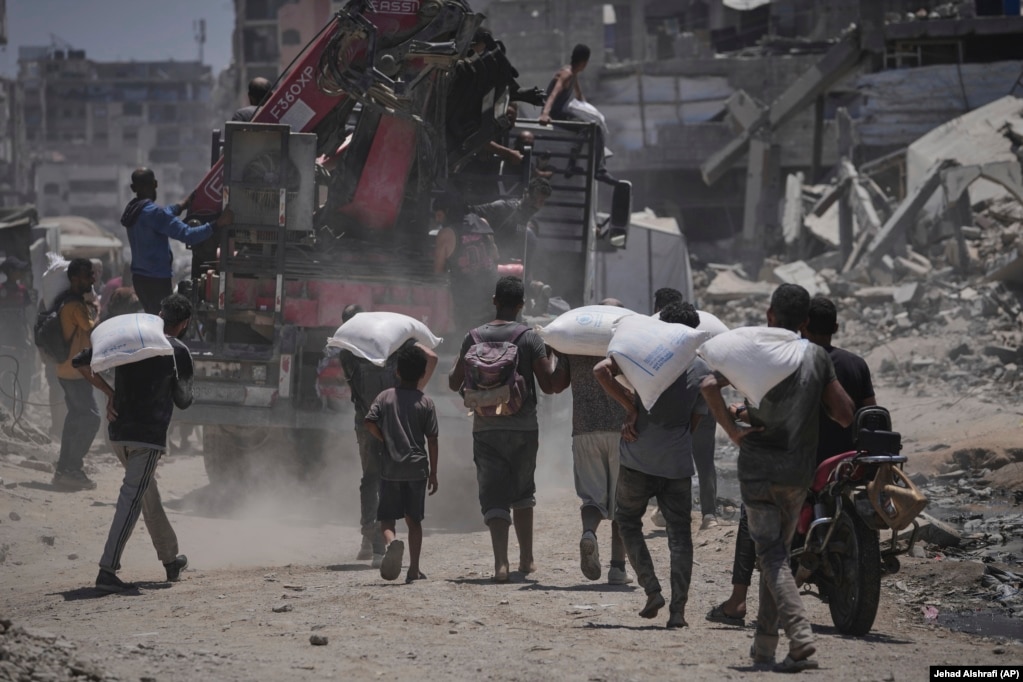 Palestinezë duke bartur thasë me miell, që i morën nga organizatat humanitare, më 22 korrik.