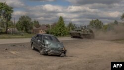 Украинская самоходная гаубица 2С1 «Гвоздика» проезжает мимо поврежденного автомобиля на дороге в Волчанском районе Харьковской области, 12 мая 2024 года