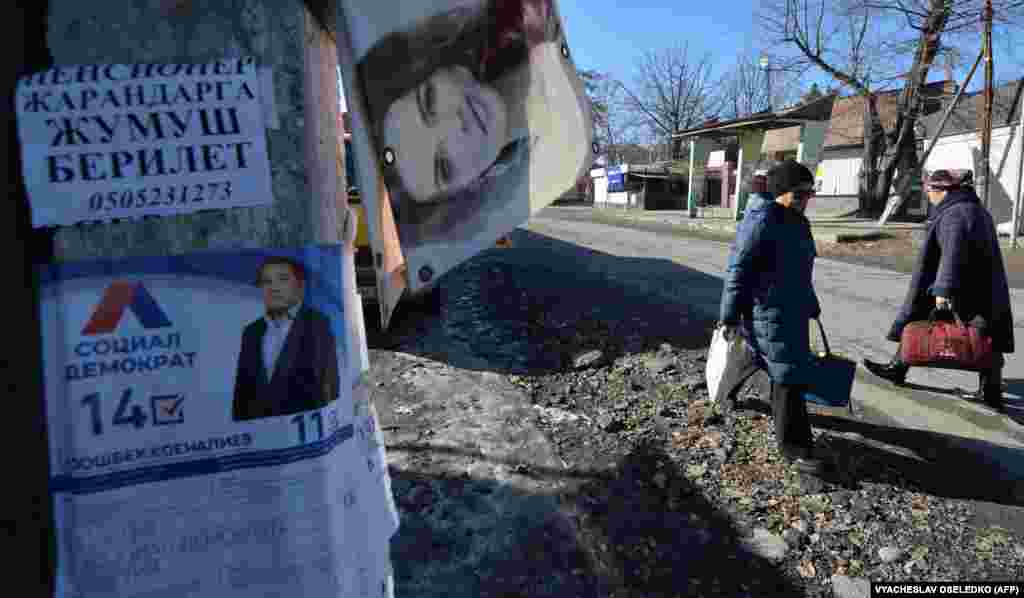 Kyrgyz women walk along a street past a campaign poster of a candidate in the upcoming parliamentary elections in the village of Tash-Dobo, some 25 kilometers from Bishkek.