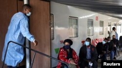 Egy egészségügyi dolgozó beszélget az emberekkel, akik a Transvaco koronavírus- (Covid–19) vakcinavonat mellett várakoznak a regisztrációra, miután a dél-afrikai Transnet vasúttársaság Covid–19-oltóközponttá alakította át a vonatot