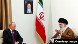 Russian President Vladimir Putin meets Iranian Supreme Leader Ayatollah Ali Khamenei during a visit to Iran in 2017. A photo on the wall shows Khamenei's predecessor, Ayatollah Ruhollah Khomeini, who founded the Islamic republic and was supreme leader until his death in 1989.