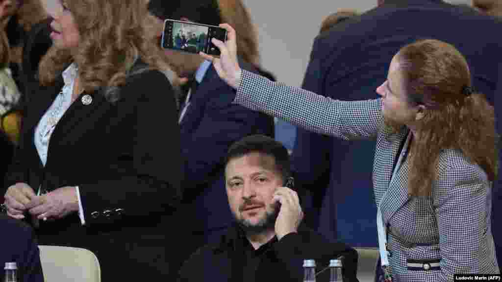 Ukrajinski predsjednik Volodymyr Zelenskyy razgovara telefonom, dok ga jedna od učesnica fotografiše mobilnim telefonom.