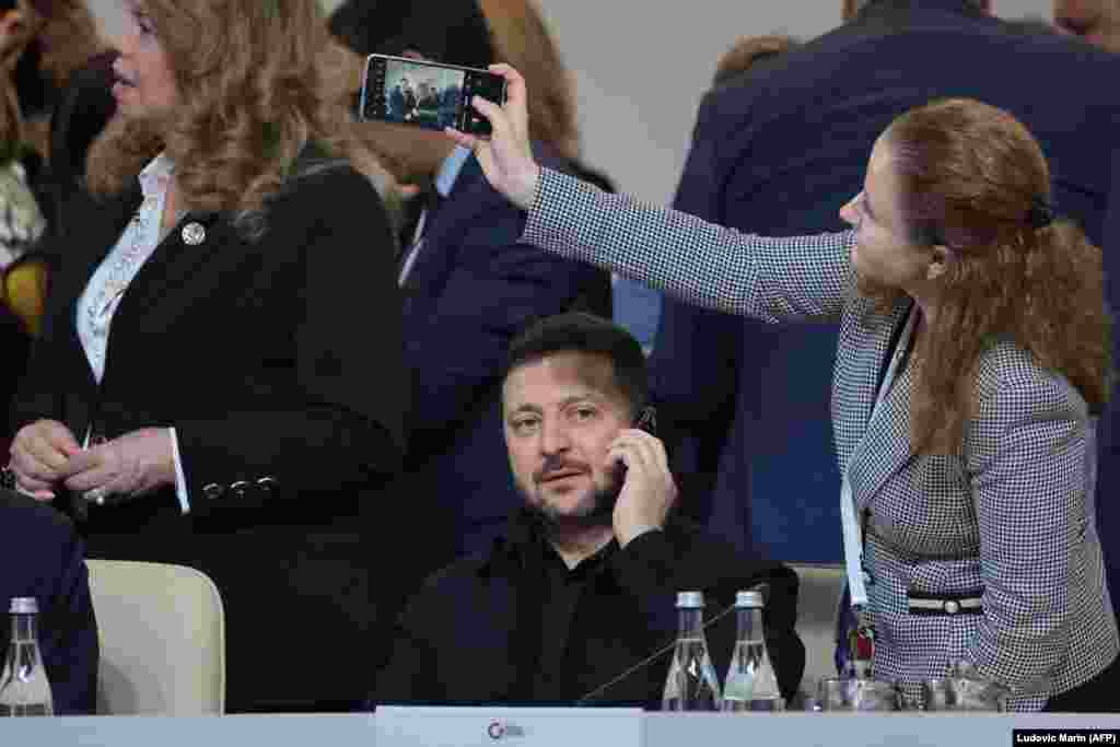 Ukrainian President Volodymyr Zelenskyy speaks by telephone as an attendee takes a cellphone photo.