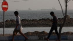 People walk at the beach, with vessels in the Strait of Hormuz visible near the beach of Bandar Abbas, Iran, August 26.