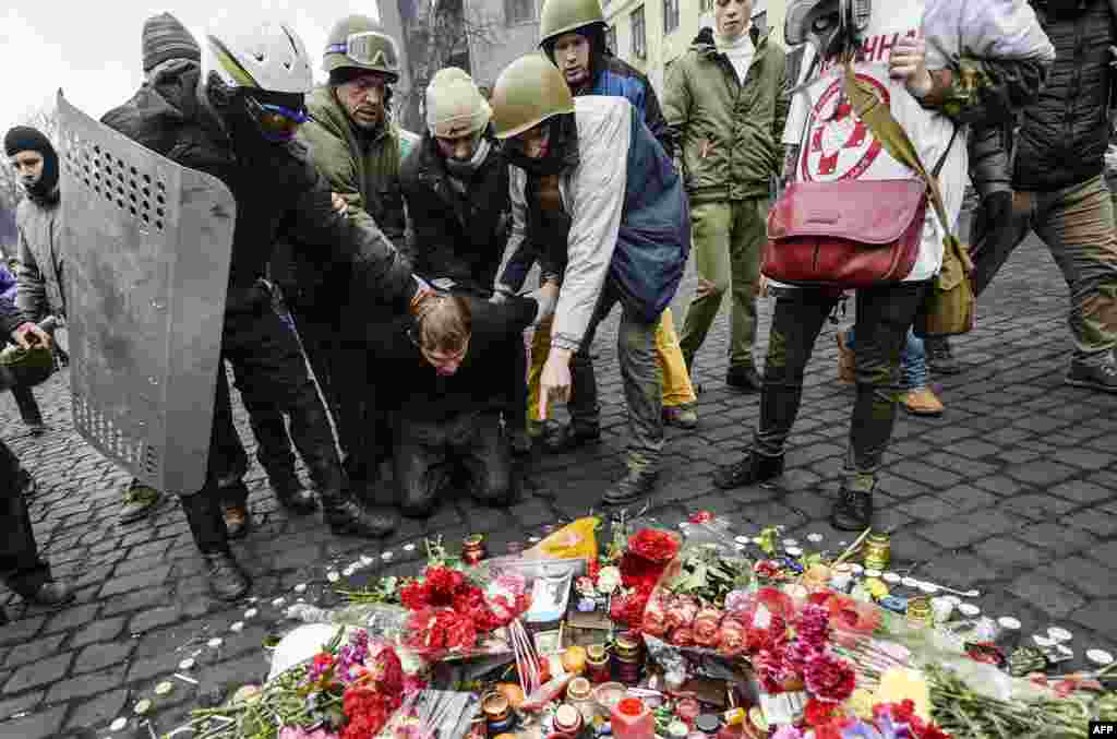 A man suspected of being a sniper for pro-government forces is forced by antigovernment protestors to pay his respects at a makeshift memorial for a victim killed during the recent violent clashes in the Ukrainian capital.