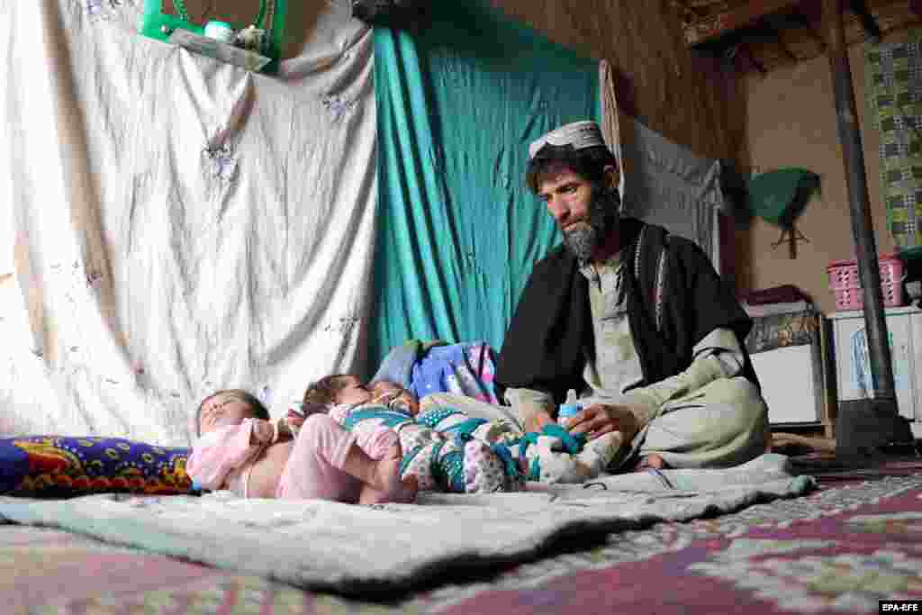 Ehsanullah, a father of newborn triplet sons, sits next to his babies at his home in Kandahar.