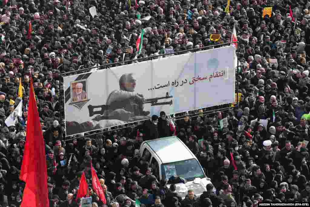 Iranian mourners carry a huge banner showing the image of Qasem Soleimani with the slogan &quot;hard revenge is on the way.&quot;