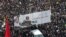 Iranian mourners carry a huge banner with poster of Qassem Soleimani and slogans reading in Persian "hard revenge is on the way". January 6, 2020