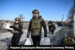 Джаред Мелоун разом поліційським несуть до евакуаційного транспорту речі людей, які виїздять з прифронтового села, Запорізька область, лютий 2026 року