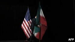 مردی در حال مرتب کردن پرچم‌های جمهوری اسلامی ایران و آمریکا در جریان مذاکرات برجام