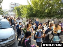 Părinții așteaptă să intre la festivitatea de deschidere a școlii.Majoritatea păstrează distanțarea socială și poartă mască la intrarea în curtea școlii