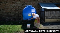 Възрастна жена пълни кофа с вода от резервоар, поставен на улицата в село Горна Студена, близо до река Дунав, по време на воден режим, 2 юли 2025 г. 
