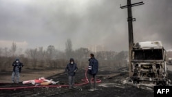 Припадник на иранската цивилна одбрана стои со црево до уништено возило-цистерна за гориво во близина на пожар што избувна по ноќниот воздушен напад врз рафинеријата за нафта Шахран во северозападен Техеран на 8 март 2026 година.