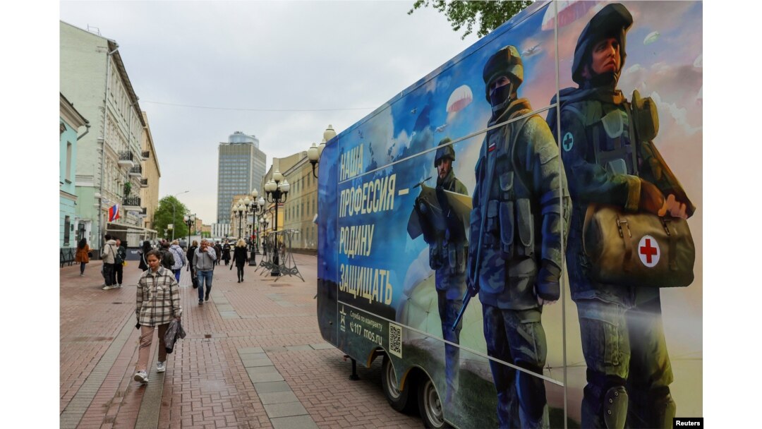Pietonii trec pe lângă un punct mobil de recrutare care promovează serviciul în armata rusă și invită voluntari să semneze un contract. Moscova, 3 mai 2023.