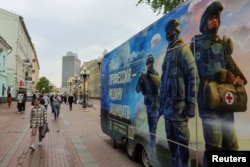 Pietonii trec pe lângă un punct mobil de recrutare care promovează serviciul în armata rusă și invită voluntari să semneze un contract. Moscova, 3 mai 2023.