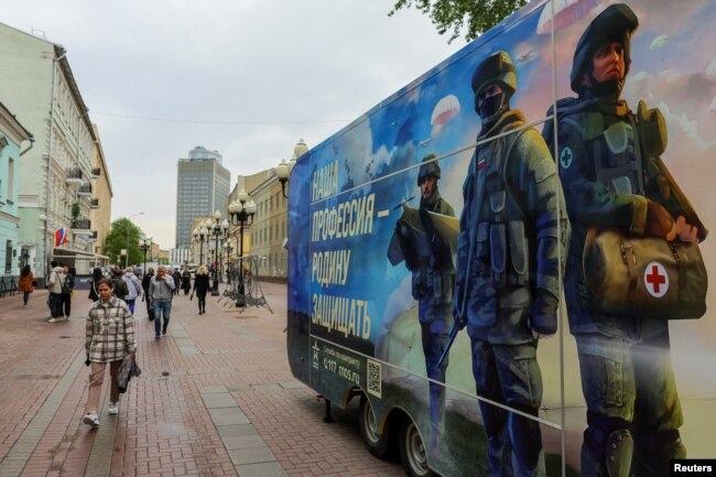 „Hivatásunk a haza védelme.” Gyalogosok sétálnak el egy mobil toborzópont mellett, amely az orosz hadseregben való szolgálatot népszerűsíti és szerződéses önkénteseket próbál verbuválni. Moszkva, 2023. május 3.