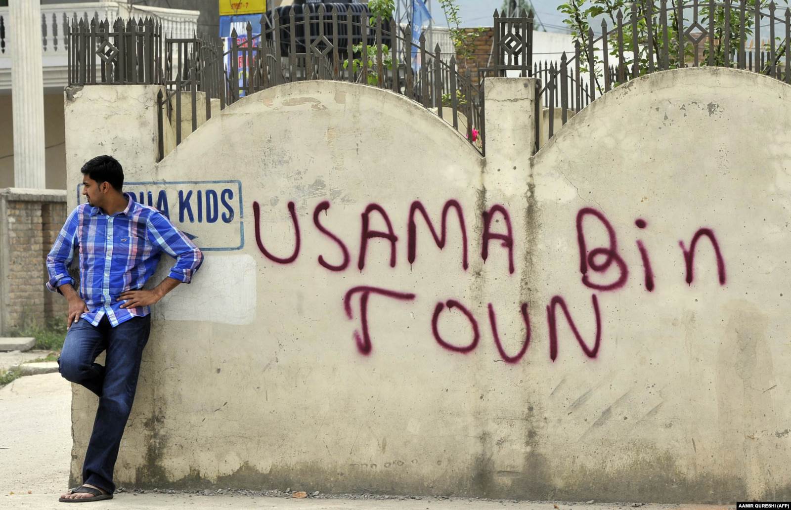Pakistanac ispred zida u Abbottabadu u blizini kompleksa u kojem se skrivao Bin Laden, na kojem piše: Osama bin grad. 
