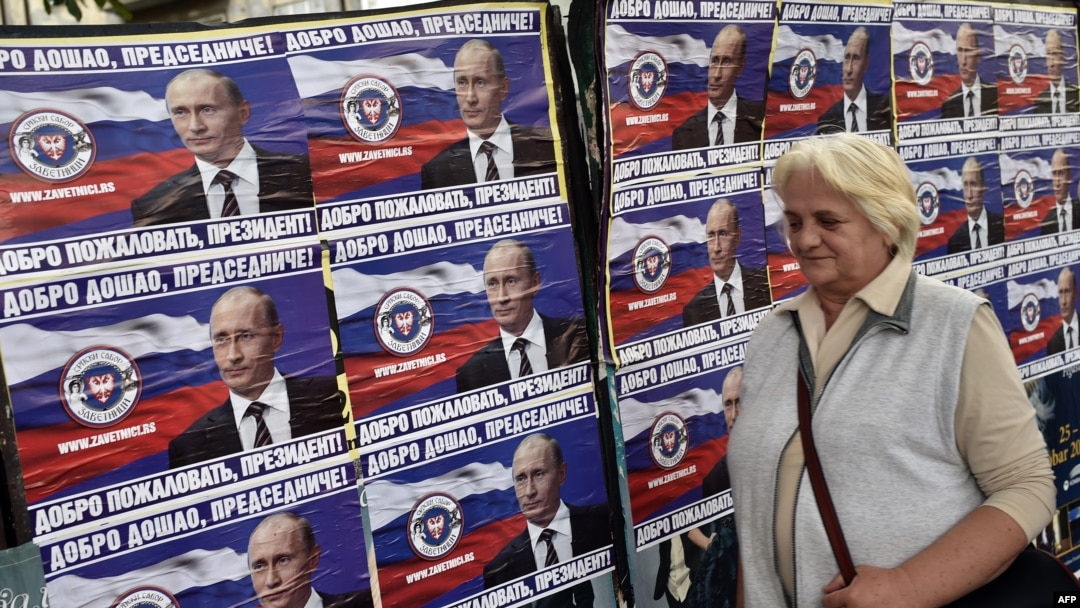 A woman walks past posters showing Russian President Vladimir Putin reading "Welcome, President" in Belgrade on October 15.