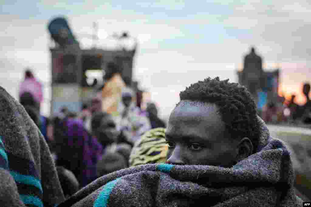 A displaced man tries to keep warm as the belongings of people fleeing violence in the Bor region of South Sudan are unloaded at Minkammen.&nbsp;(AFP/Nichole Sobecki)