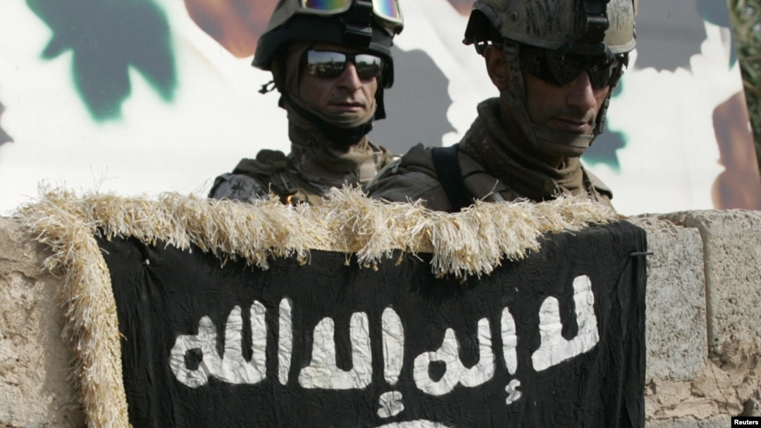 Soldiers look at the flag of Al-Qaeda militants on the wall of a house that used to be a weapons cache in western Baghdad. (file photo)