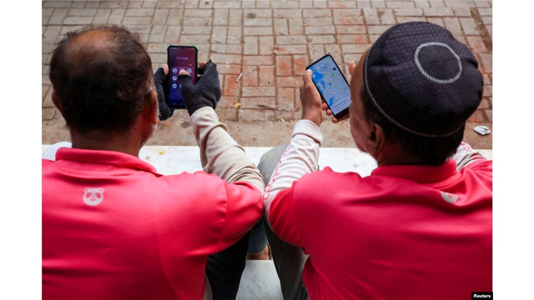 Riders check their mobile phones for online food orders from customers while waiting outside an office in Karachi. (file photo)