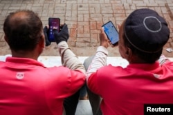 Riders check their mobile phones for online food orders from customers while waiting outside an office in Karachi. (file photo)