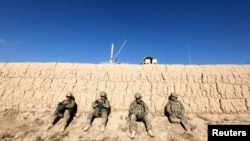 FILE: U.S. soldiers sit behind a wall as others search for explosives after an IED (improvised explosive device) blast damaged one of their armoured vehicles during a road clearance patrol in Logar province.