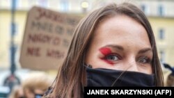 Žena na protestima u Varšavi nosi masku s usvojenim simbolom crvene munje (28. oktobar 2020.)