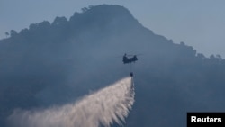 Un elicopter Chinook aruncă apă pe focarele de incendiu din munții Kitheronas, deasupra localității Psatha, Grecia, pe 4 august 2026.
