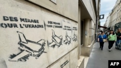 Pietoni trec pe lângă un graffiti care evidențiază recentul anunț potrivit căruia avioane Mirage din Franța vor fi trimise în Ucraina, pictat pe un zid de pe Rue Saint-Anne, în centrul Parisului, la 20 iunie 2024.