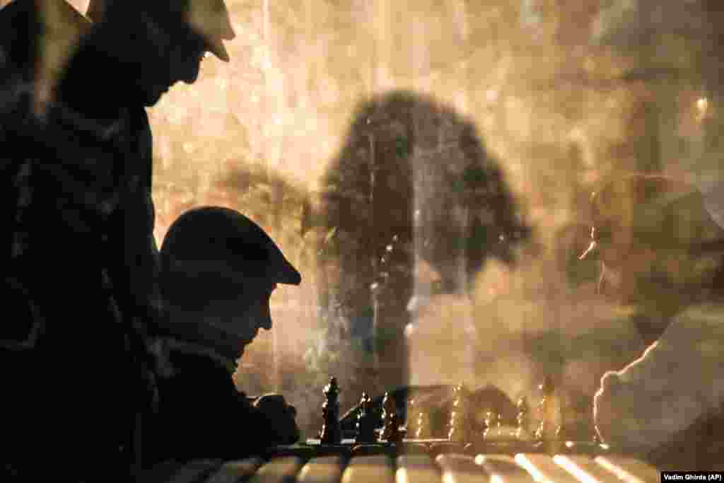 Men play chess, lit by the setting sun, while others watch in a park in Bucharest, Romania. (AP/Vadim Ghirda)