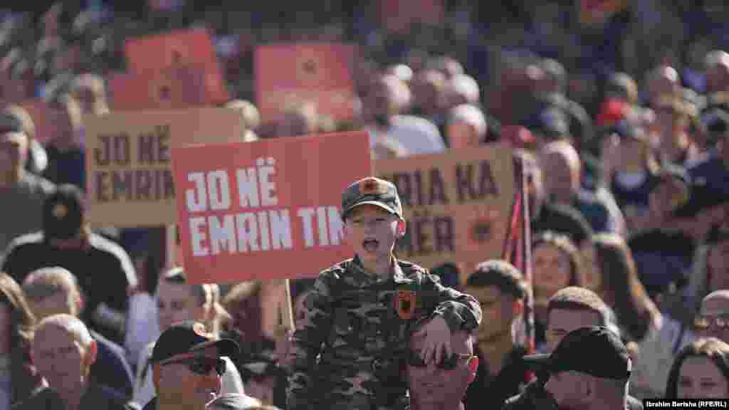 Një djalë i ri i veshur në uniformë të UÇK-së brohorit teksa në prapavijë shihen pankarta me mbishkrimin: "Jo në emrin tim", "Liria ka emër", në protestën kundër aktgjykimit të Hagës për dënimin e ish-udhëheqësve të UÇK-së me burgim për krime lufte.