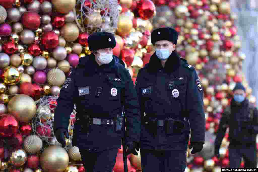 Moscow police officers wear face masks as they patrol past Christmas decorations.