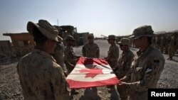 Canadian Army soldiers fold the national flag during a ceremony marking the Canadian handover of forward fire base Zangabad to U.S. forces in Kandahar Province on June 19.