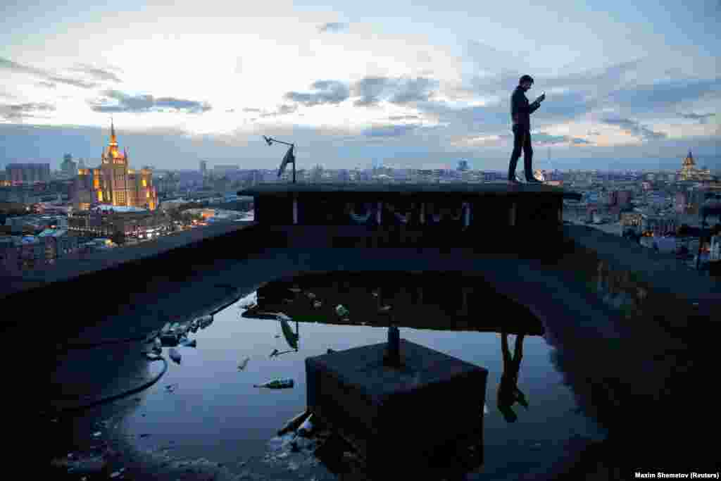 Sergei Rodionov of team &quot;Rudex&quot; takes a photograph on his mobile phone from a rooftop in Moscow. His small group is nonpolitical, but it has shown concern for urban renewal by posting pictures of decaying buildings on social media.