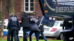 Egy gyanúsítottat kísérnek a rendőrök, miután megérkezett a németországi Karlsruhéba 2022. december 7-én, szerdán. Több ezer rendőr hajtott végre razziákat Németország nagy részén a feltételezett szélsőjobboldali szélsőségesek ellen, akik állítólag fegyveres puccsot akartak indítani