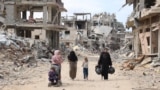 Palestinian women and children walk on a dirt road lined with building rubble in Gaza City on October 7, the first anniversary of Israel's war in the Gaza Strip.