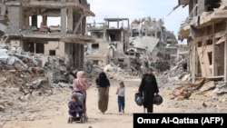 Palestinian women and children walk on a dirt road lined with building rubble in Gaza City on October 7, the first anniversary of Israel's war in the Gaza Strip.