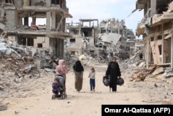 Palestinian women and children walk along a road lined with rubble in Gaza City on October 7, 2024, the first anniversary of Israel's ongoing war in the Gaza Strip.