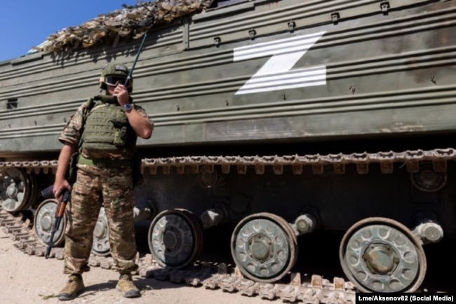 Російський військовослужбовець на тлі військової техніки із Z-символікою