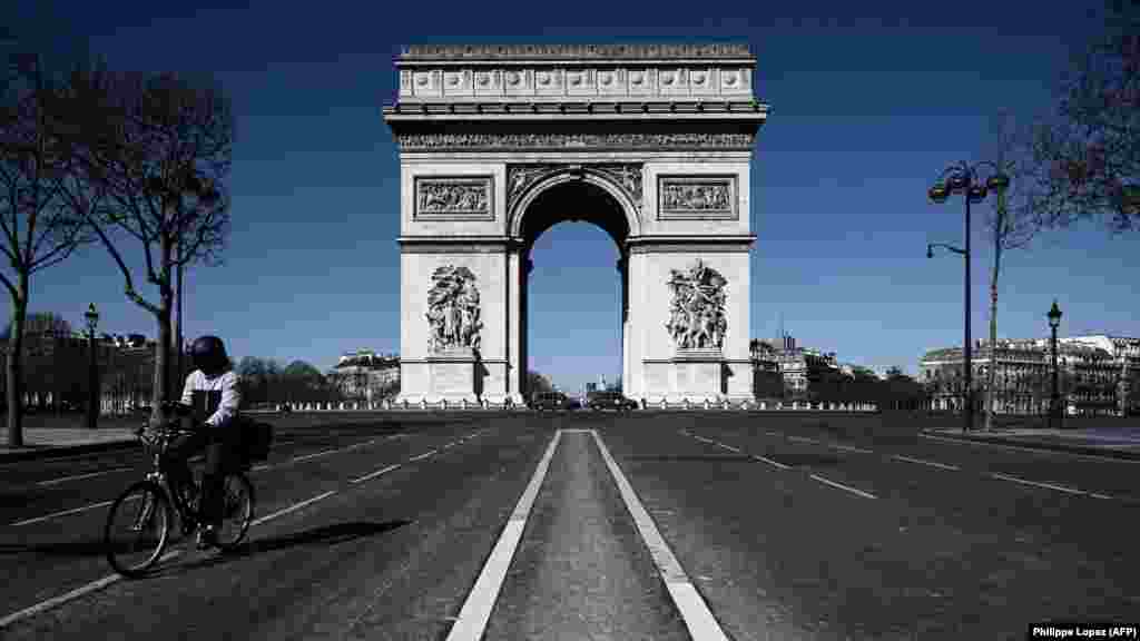 France - A man rides his bicycle past the Arc de Triumph in Paris, 23Mar2020
