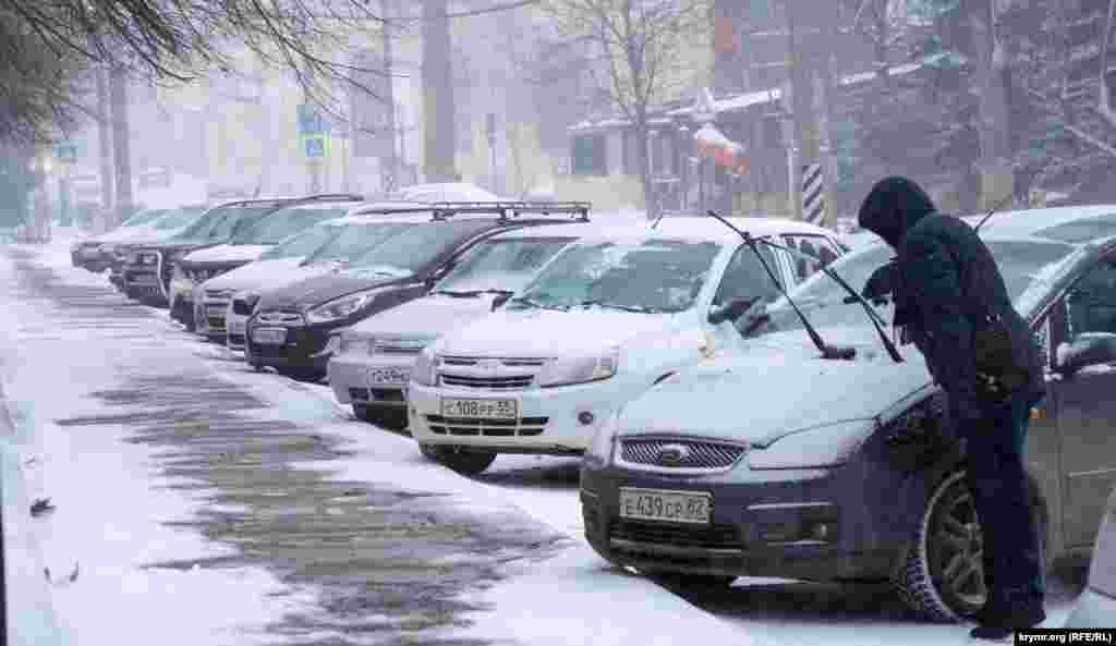 Чоловік очищає від снігу свій автомобіль на стоянці біля будівлі парламенту Криму