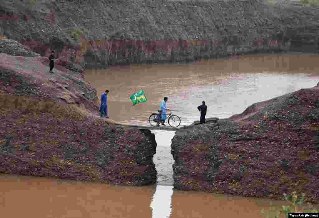 A man crosses a stream on his bicycle with a political-party flag on the outskirts of Peshawar, Pakistan. (Reuters/Fayaz Aziz)