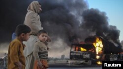 Pakistanis watch fuel trucks that were set ablaze in the Bolan district of Baluchistan Province on December 12.