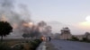 FILE: Afghan men watch the aftermath of a suicide car bomb attack on a military base in Khost.