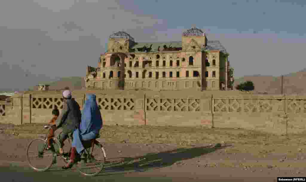 A family rides past the destroyed Darull Aman Palace.