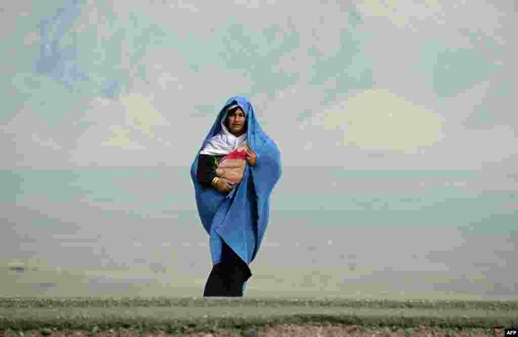 An Afghan woman holding her child waits for transportation on the outskirts of Herat. (AFP/Aref Karimi)