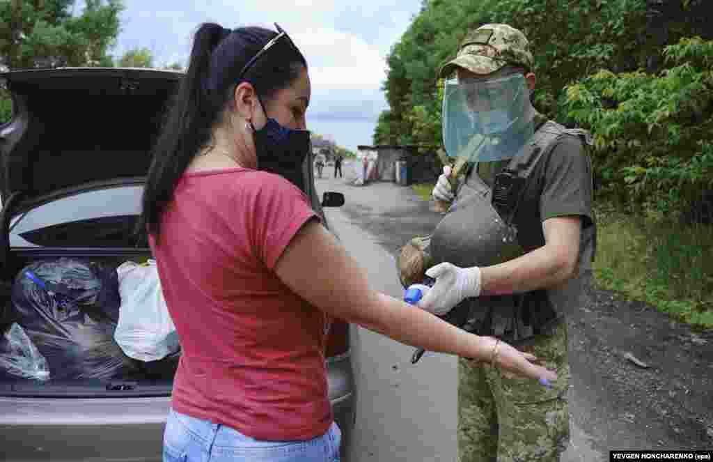 Украинский военный измеряет женщине температуру на блокпосту между территориями, контролируемыми Киевом, и землями, подконтрольными пророссийским сепаратистам. Окрестности Донецка, 22 июня.