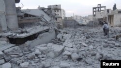 Residents stand near buildings damaged by what activists said were missiles fired by a Syrian Air Force fighter jet loyal to President Bashar al-Assad in Binsh near Idlib on January 2.