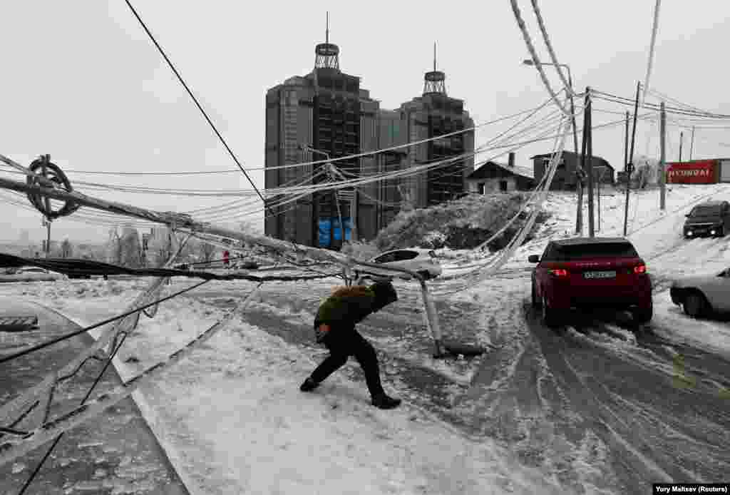 A man walks under a damaged pylon, covered with ice after freezing rain, in the Russian city of Vladivostok. (Reuters/Yuri Maltsev)